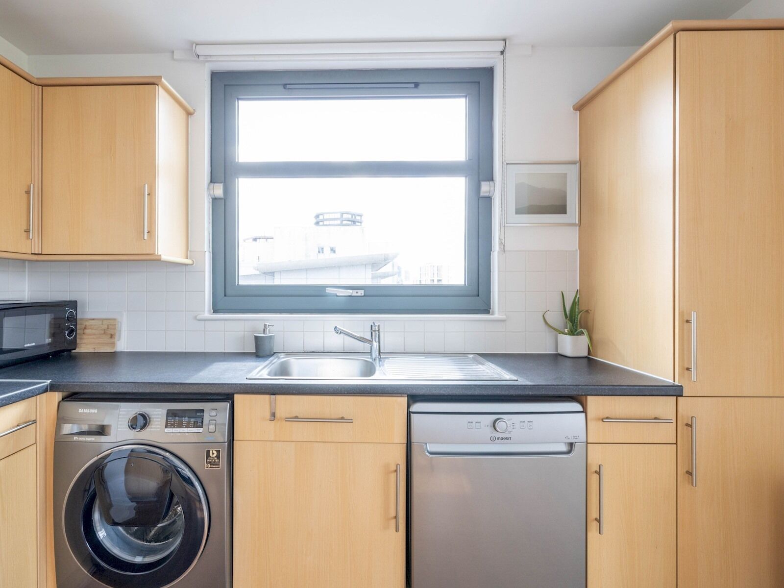 Une cuisine moderne avec des meubles en bois, un four à micro-ondes encastré, un lave-linge et un lave-vaisselle.