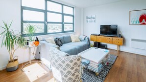A modern living room with a large window, a sofa, a coffee table, and a TV on a wooden cabinet. - Central Location Flat near Old St and Dalston Overlooking Rosemary Park and Regents Canal - Pass the Keys (London)