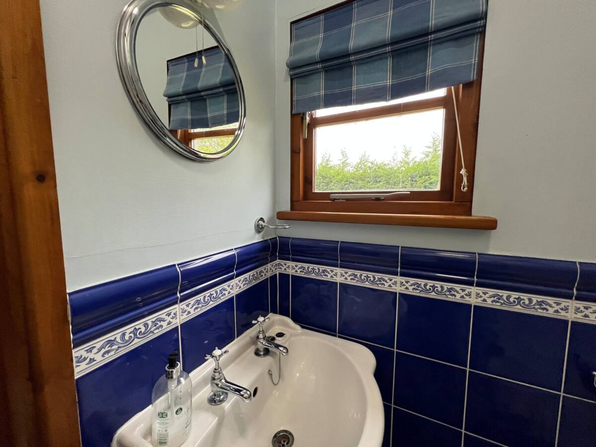 A bathroom with a white sink, two faucets, a mirror, and a window with blue blinds.