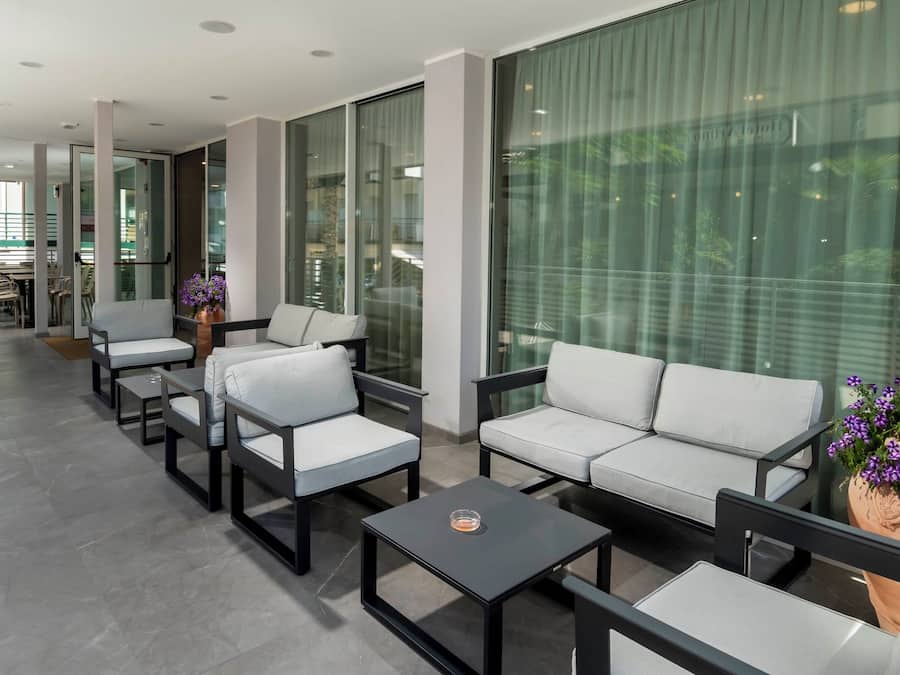 A modern lounge area with sofas and tables, large windows, and potted plants.