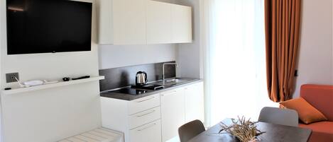A modern kitchen with white cabinets, a flat-screen TV, and a dining area with a table and chairs.