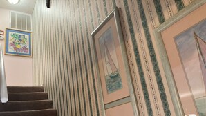 Una escalera con papel tapiz a rayas, un cuadro enmarcado de un velero y un mural de peces de colores en la pared.
