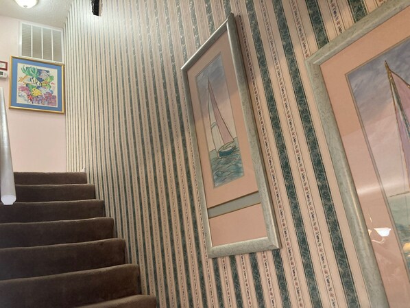 Una escalera con papel tapiz a rayas, un cuadro enmarcado de un velero y un mural de peces de colores en la pared.