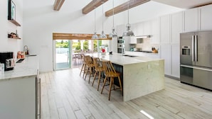 Une cuisine moderne avec des meubles blancs, un îlot en marbre, des tabourets de bar en bois et des appareils électroménagers en acier inoxydable.