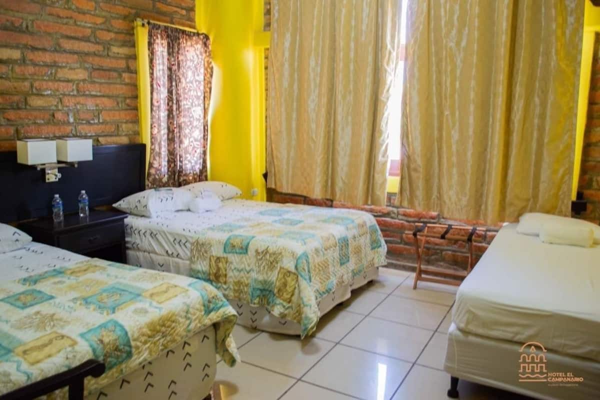 Een hotelkamer met twee bedden, een bakstenen muur, een gele accentmuur en een raam met gordijnen.