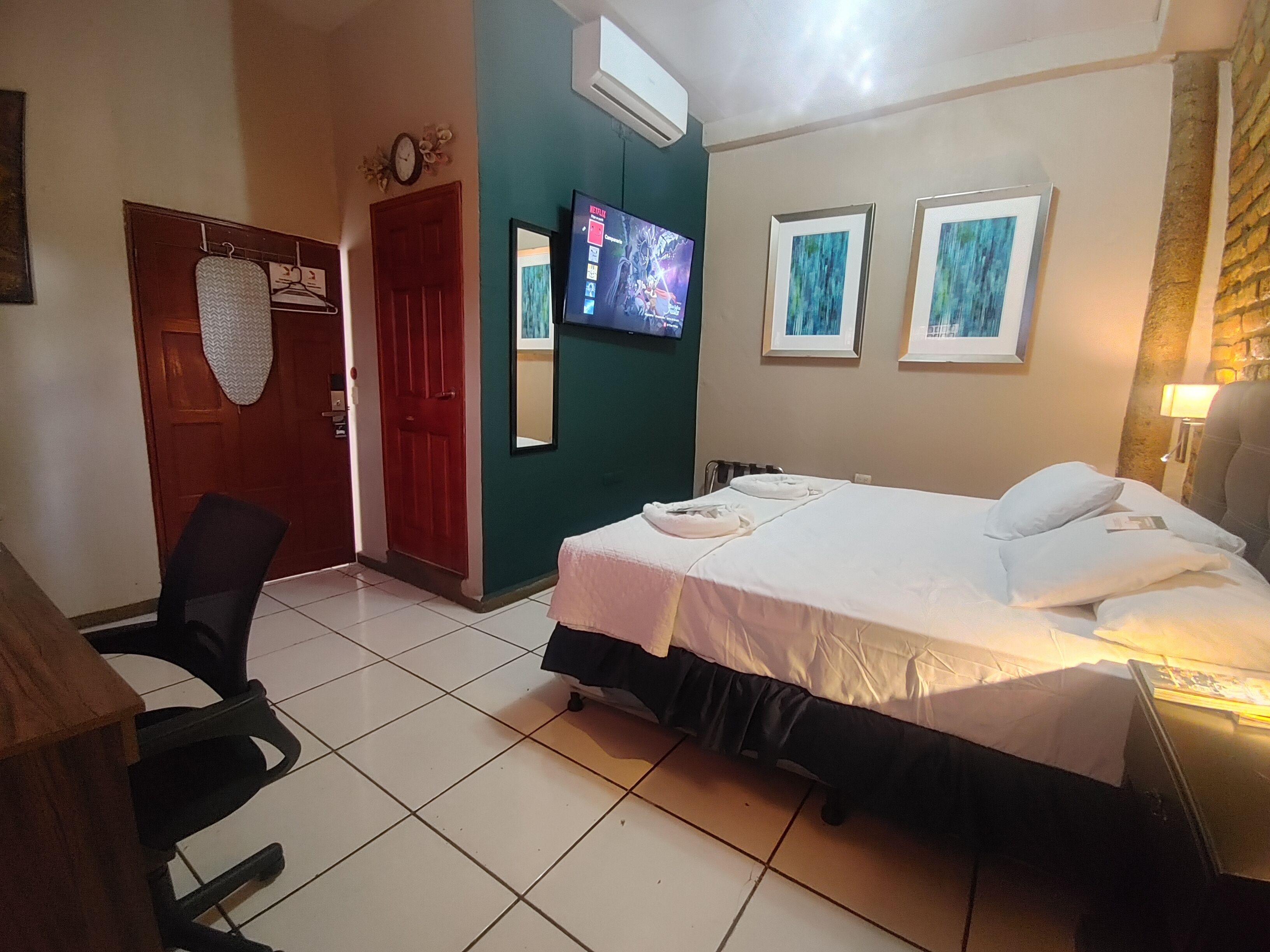 A hotel room with a bed, a TV mounted on the wall, and a door with a towel rack.