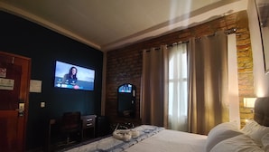 A hotel room with a bed, a desk, a television, and a stone wall.