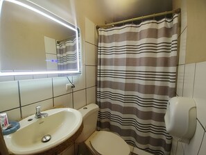 A bathroom with a white sink, a toilet, a striped shower curtain, and a mirror with a light. - Hotel El Campanario (Comayagua)