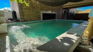 A swimming pool with clear water, surrounded by a brick wall and a stone deck.