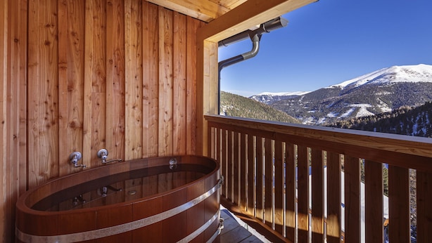 Eine Holzhütte mit Badewanne aus Holz und Blick auf einen schneebedeckten Berg.