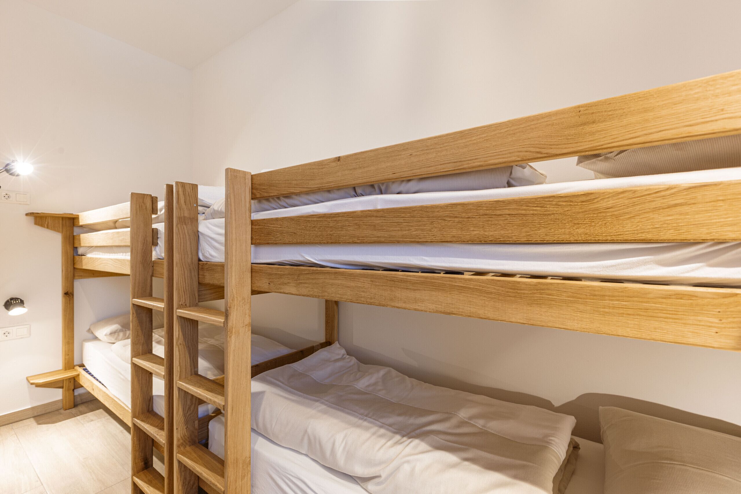 Een stapelbed met houten frames en wit beddengoed.