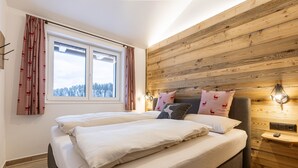 Ein Schlafzimmer mit einer Holzwand, einem großen Bett mit weißer Bettwäsche und einem Fenster mit Vorhängen.