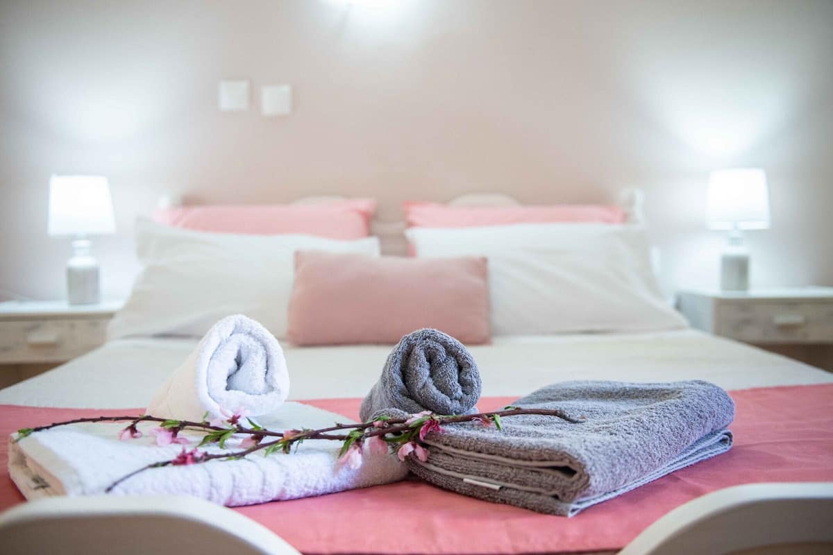 A neatly made bed with pink and white bedding, two bedside lamps, and a branch with pink flowers on the bed.