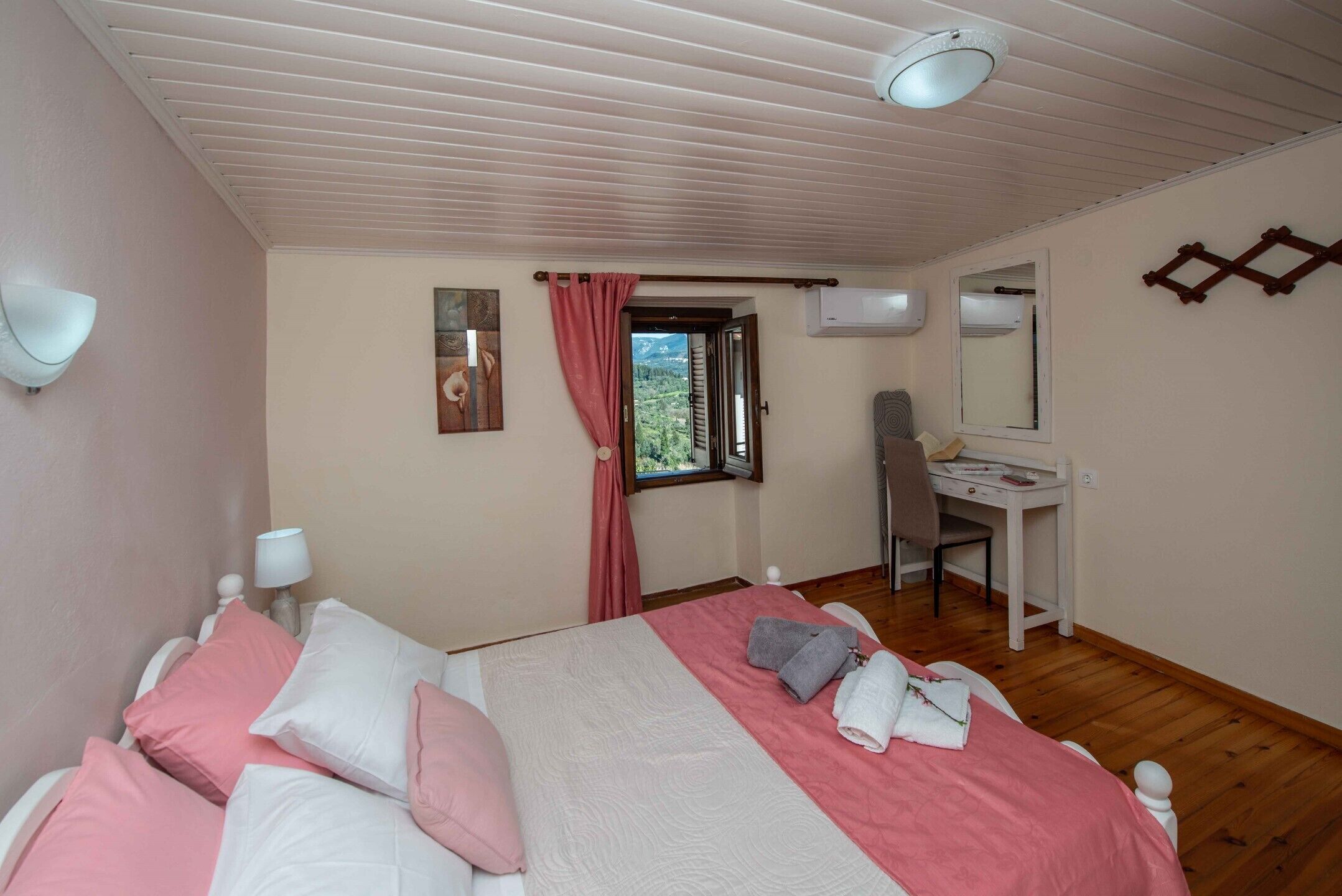 A bedroom with a bed, a desk, and a window with a view of greenery.