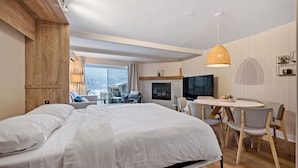 Una camera d'albergo moderna con un letto grande, un'area pranzo con un tavolo rotondo e sedie, una TV e un caminetto.