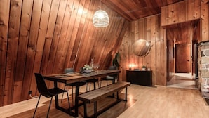 A dining area with a wooden table, chairs, and a bench. There is a hanging light fixture above the table.
