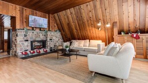 A cozy living room with a stone fireplace, a white sofa, and a television mounted on the wall.