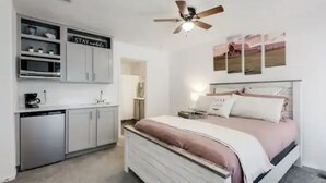 A bedroom with a bed, a ceiling fan, a kitchen area with cabinets, and a sign that says "STAY and relax". - Cozy Mountain Town Farmhouse for Winter Fun in Flag!  (Flagstaff)