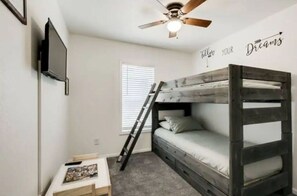 Dormitorio con literas, ventilador de techo, escalera, una pequeña mesa con un cuadro y una pared que dice 'Follow Your Dreams'.