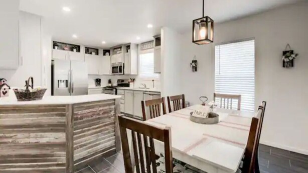 A modern kitchen with white cabinets, a central island, and a dining area with wooden chairs and a table. - Cozy Mountain Town Farmhouse for Winter Fun in Flag!  (Flagstaff)