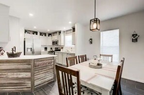 Una cocina moderna con armarios blancos, una isla central y una zona de comedor con sillas y mesa de madera.