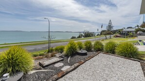 Un espacio exterior ajardinado con vista al mar, un camino pavimentado y un edificio moderno al fondo.