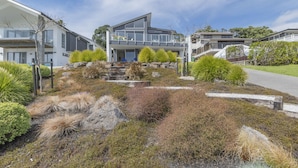 Una casa moderna de dos pisos con balcón, rodeada por un jardín ajardinado con arbustos diversos y un sendero de piedra.