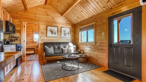 A cozy cabin interior with wooden walls, a sofa, a dining table, and a kitchen area.