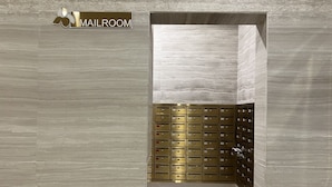 A modern mailroom with a marble wall and a gold-colored mail slot system.