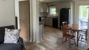 Una cocina moderna con armarios blancos, un refrigerador negro y una zona de comedor con una mesa y sillas de madera.