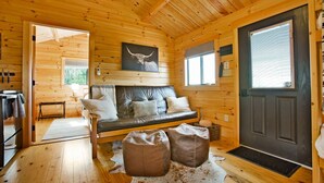 A cozy cabin interior with a leather sofa, wooden walls, a mounted artwork, and a door with a window. - Sanctuary Summit | Hot Tub, Panoramic Views, ADA Friendly Cabin (Brookville)