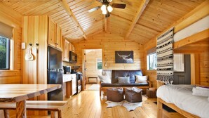 A wooden cabin interior with a dining table, kitchen area, and a bed. - Sanctuary Summit | Hot Tub, Panoramic Views, ADA Friendly Cabin (Brookville)