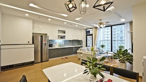 A modern kitchen with stainless steel appliances, a dining area with a white table, and a living space with a sofa and chairs.