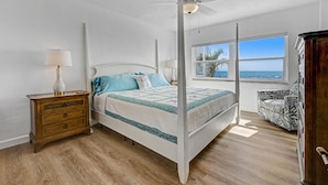Un dormitorio con cama con dosel, una mesita de noche, una silla y una ventana con vistas al océano.