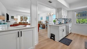 Una cocina moderna con armarios blancos, una isla central y vistas al área de estar.