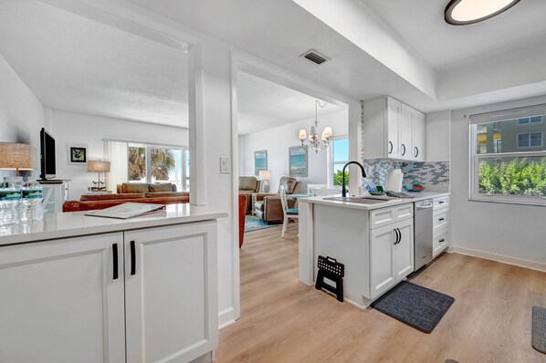 A modern kitchen with white cabinetry, a central island, and a view of the living area.