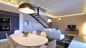 Un salon moderne avec un escalier, un coin repas doté d’une table ronde et un téléviseur en arrière-plan.