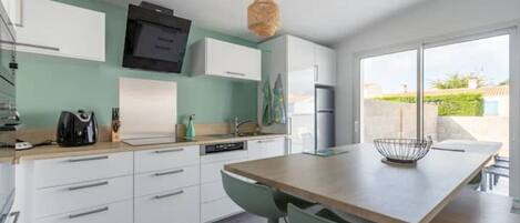 A modern kitchen with white cabinets, a wooden countertop, and a dining area with a table and chairs.