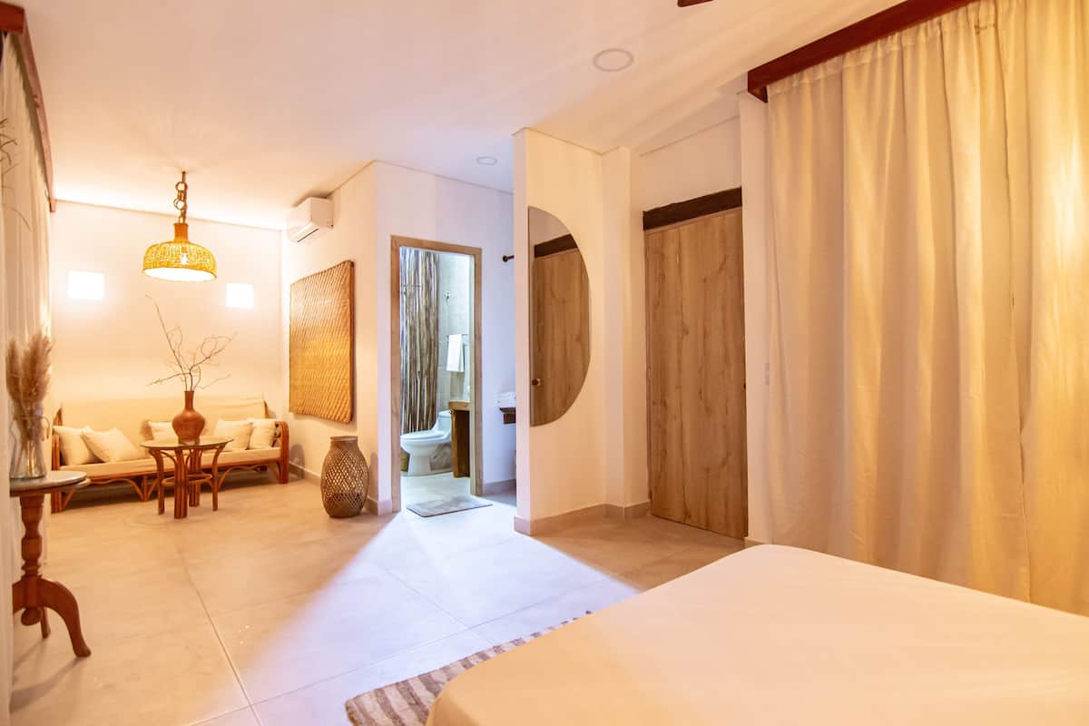 Ein Hotelzimmer mit Bett, Sofa, Esstisch und einem durchgehenden Türspalt sichtbaren Badezimmer.