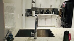 Een moderne keuken met witte kasten, een roestvrijstalen spoelbak en een zwarte koelkast.