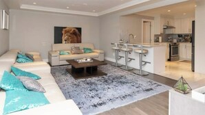 Een moderne woonkamer met een bank, salontafel en een groot schilderij van een leeuw. Er is een keuken met een bar en een spoelbak.