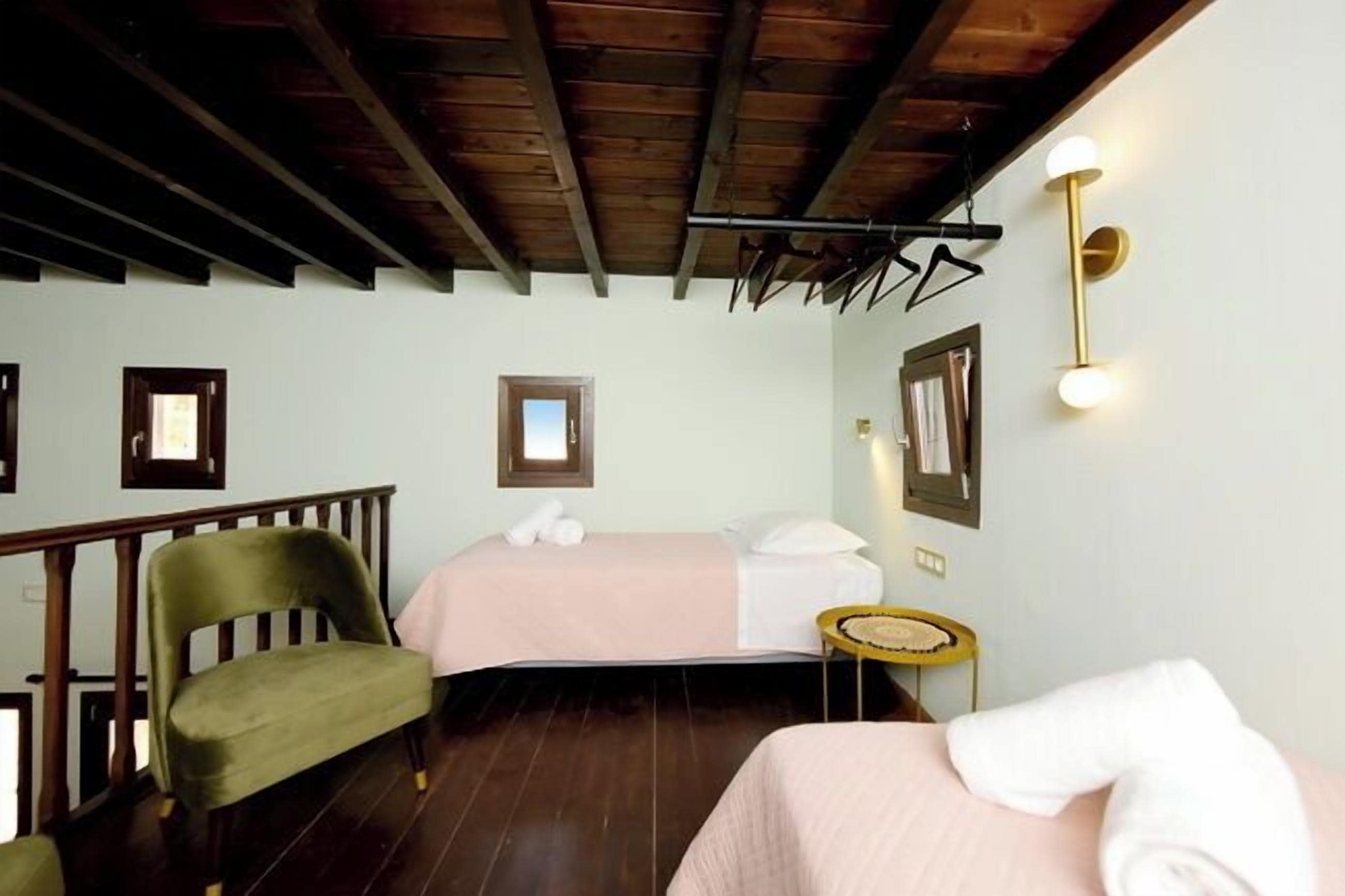 Une chambre avec deux lits, une chaise en bois, une petite table et un luminaire fixé au mur.