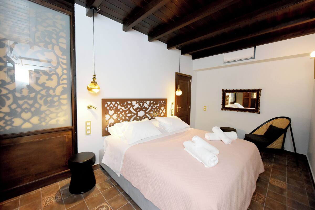 Quarto de hotel com uma cama, mesa de cabeceira, uma cadeira e um espelho.