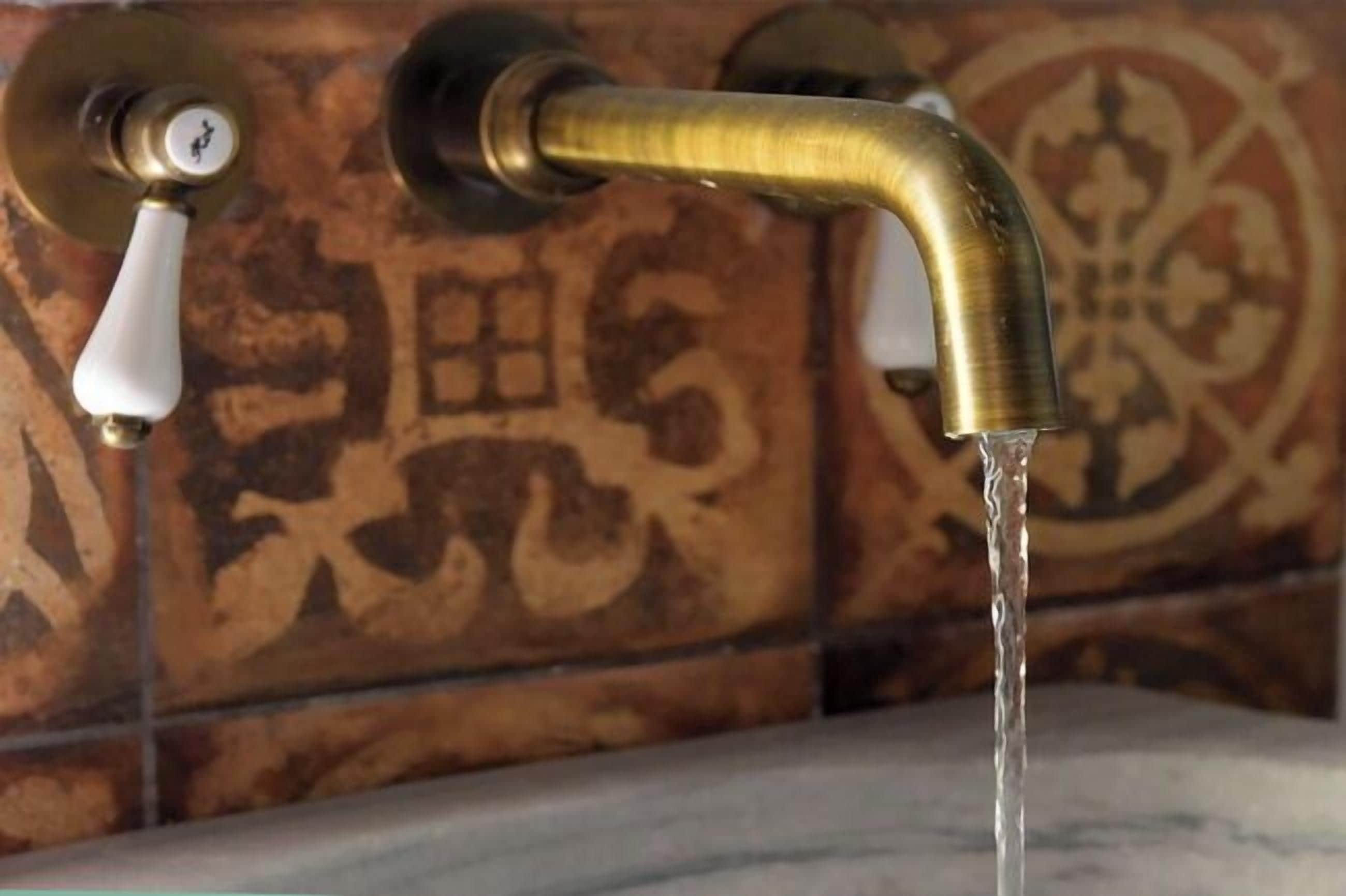 Een badkamer met een messing kraan en een wand betegeld met decoratieve tegels.