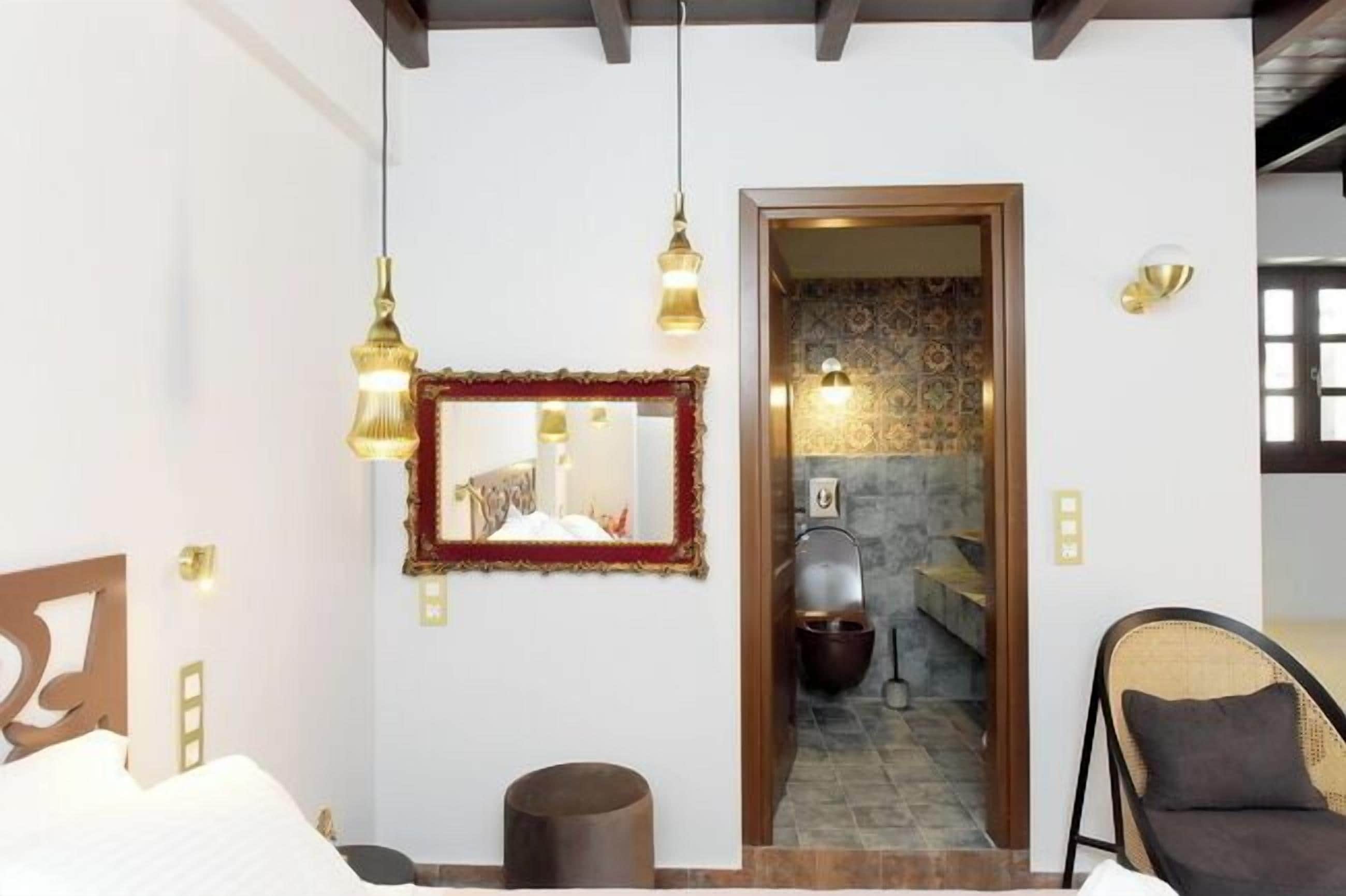 Une chambre d’hôtel avec un lit, une chaise, un miroir et une salle de bain visible à travers une porte ouverte.
