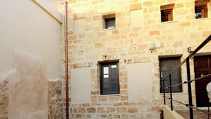 A narrow courtyard with a stone wall, a small window, and a door leading to a tiled area. - Elaia-Fos (Rhodes)