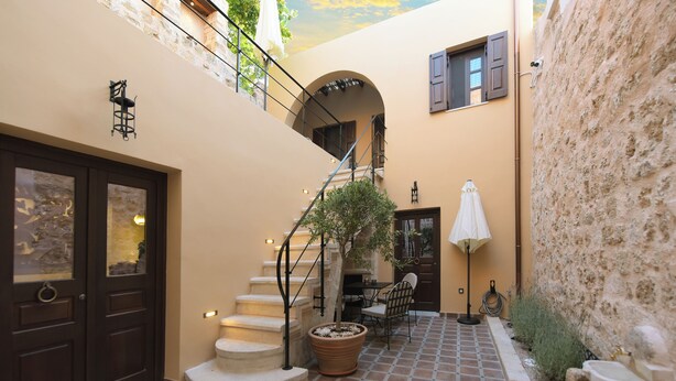 A courtyard with a staircase, a door, a potted plant, a table with chairs, and a lamp. - Elaia-Fos (Rhodes)