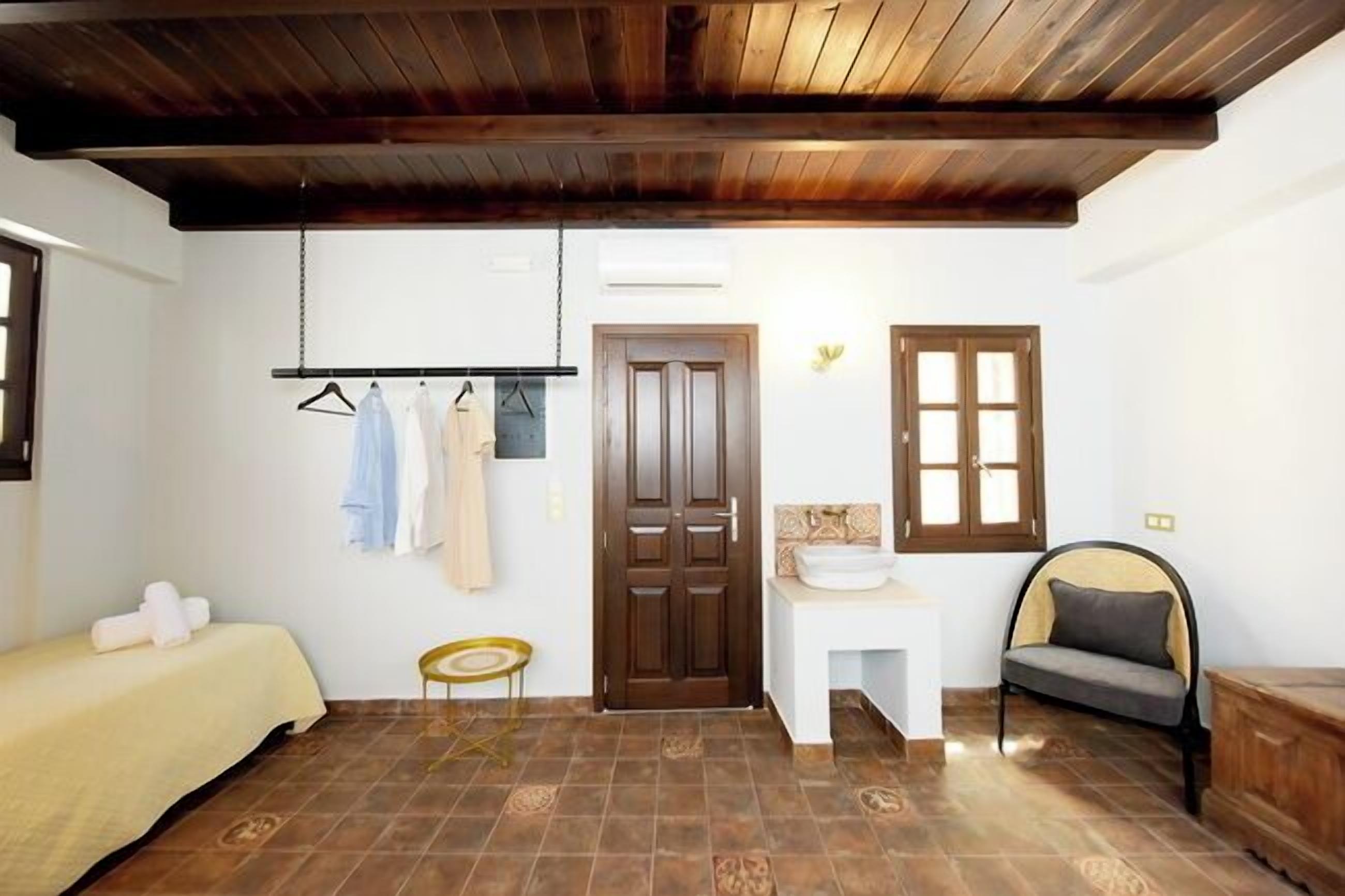 A room with a bed, a small table, a chair, a hanging clothes rack, and a door.