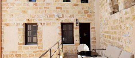 A stone building with a balcony, a door, and a small table with chairs.