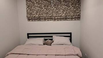 A bedroom with a bed, a headboard, and a patterned curtain.